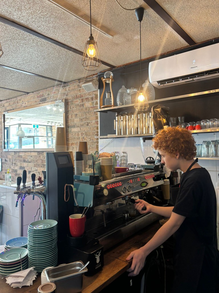 Eli Searle working as a barista at an espresso machine in a warm brick-walled café